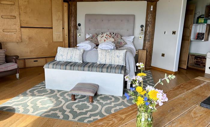 Inside Saffir Lodge, warm light fills a rustic open-plan space with wooden beams, soft furnishings and floral touches. A cozy armchair and natural tex